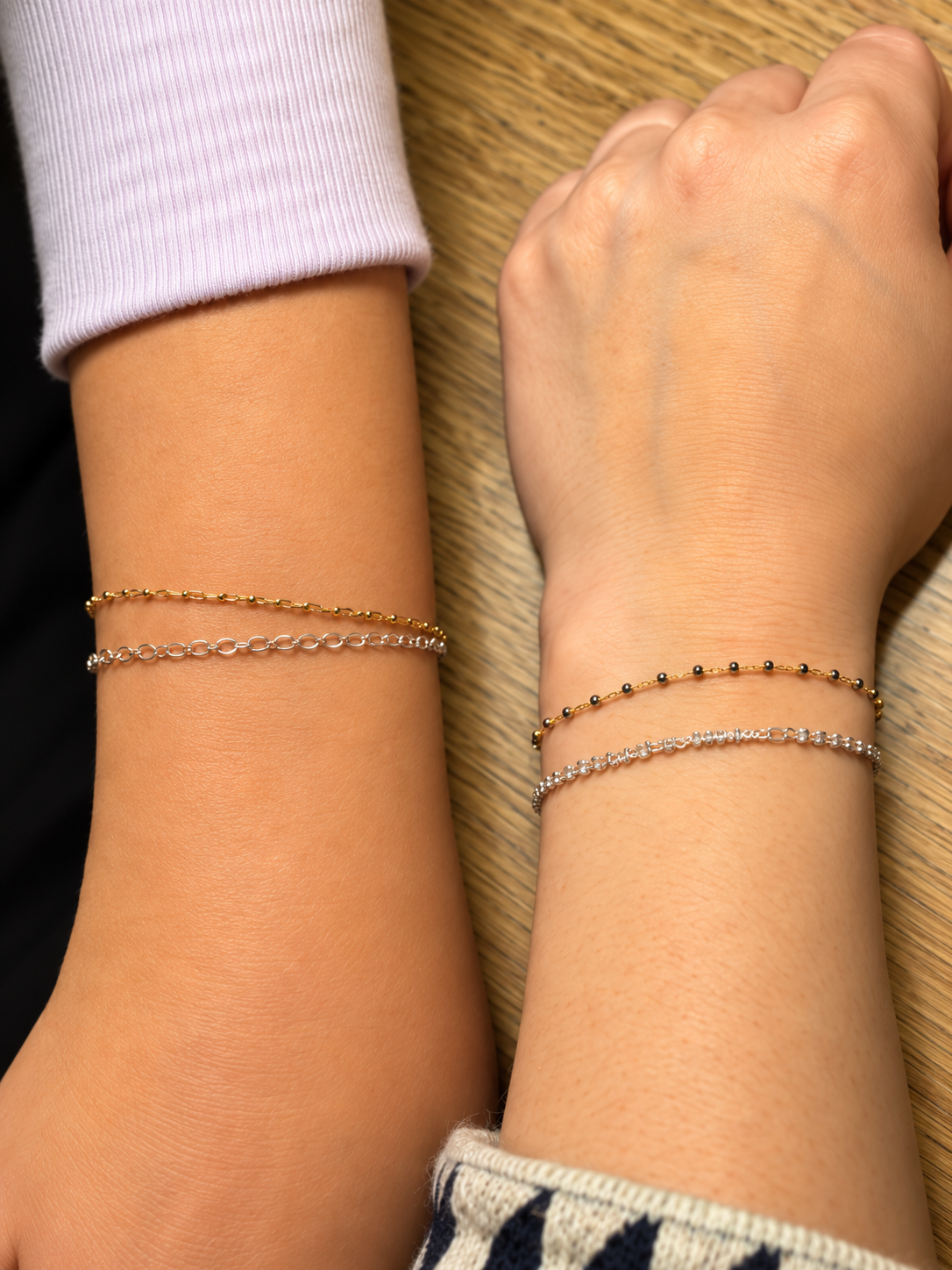 Two wrists wearing delicate gold and silver chain bracelets by Abby